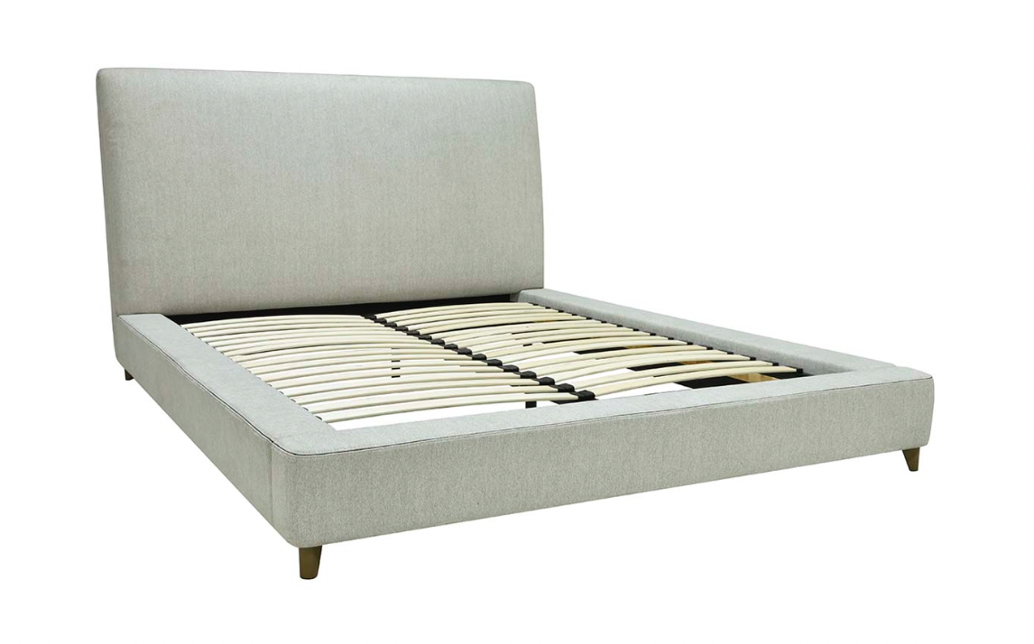 A fully upholstered oatmeal-colored bed with a streamlined, low platform design and dark brown tapered legs.
