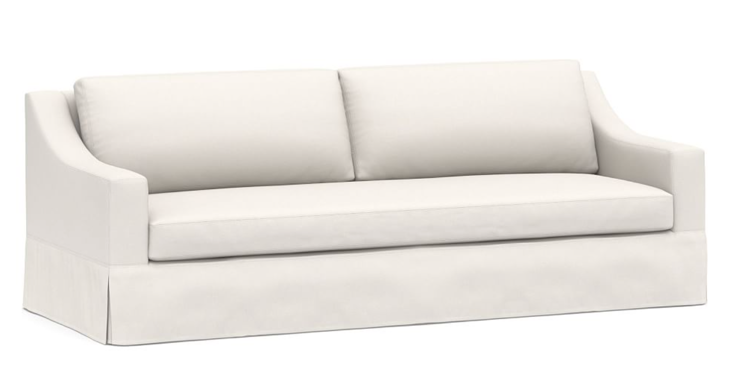 A white slipcovered sofa with graceful, sloping arms and a cushioned backrest.